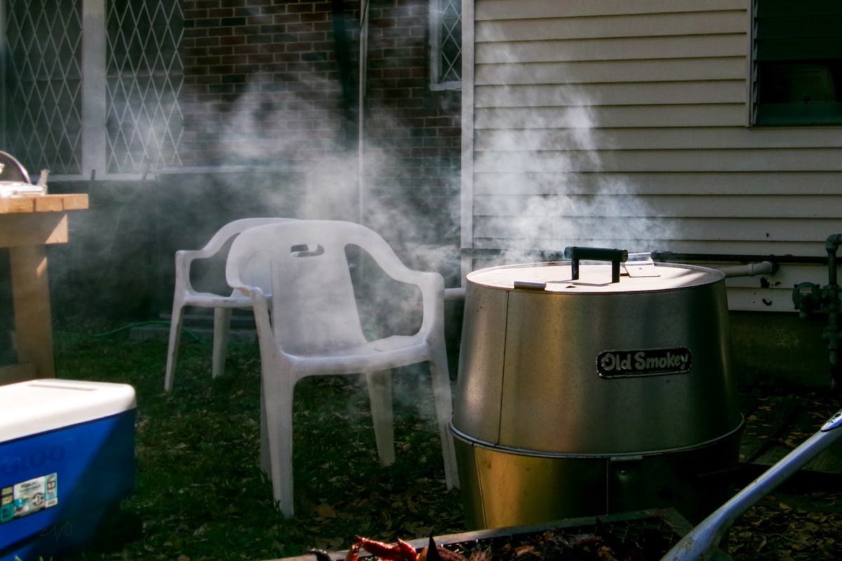 Backyard charcoal smoker with smoke billowing during an outdoor cook
