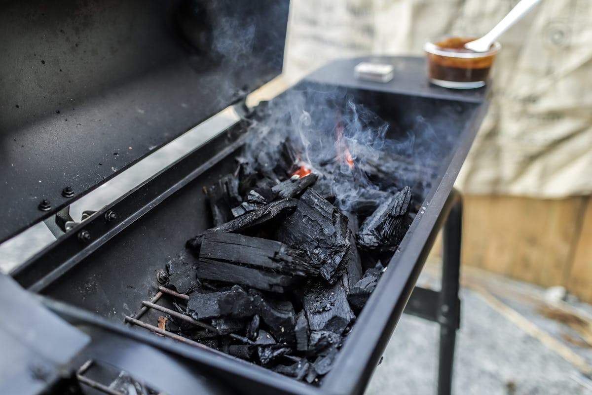 Close-up of a charcoal grill with lit coals and smoke rising