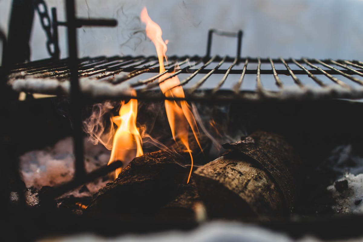 Firewood burning in a fire pit with a metal grill grate above for smoking and grilling