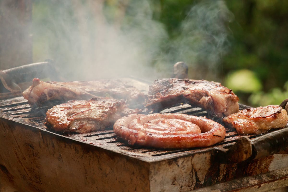 Sausages and meat smoking on a BBQ grill with visible smoke