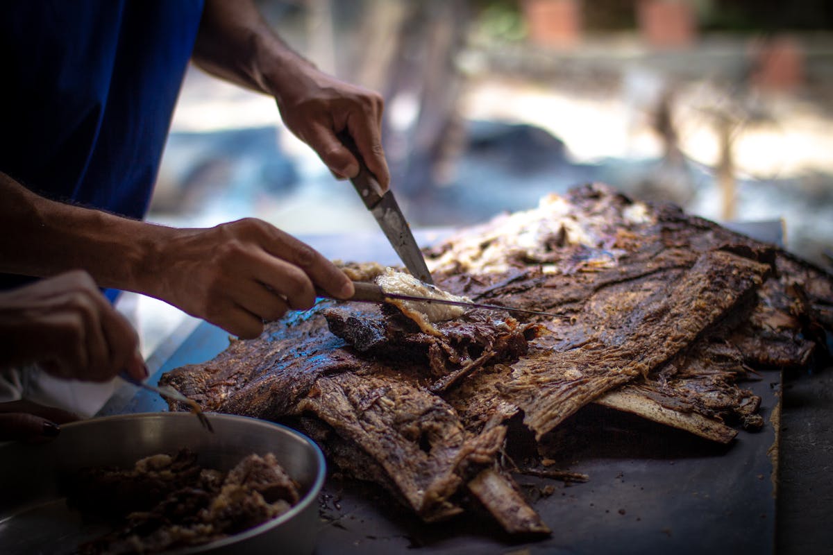 Cook slicing tender smoked beef short ribs on a rustic table