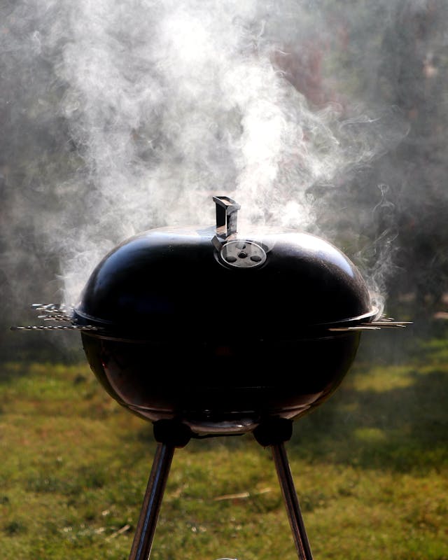 Classic charcoal grill emitting smoke outdoors on a sunny day