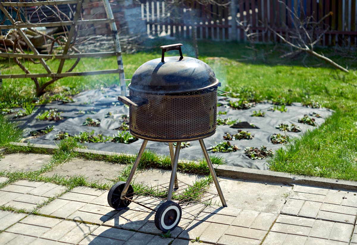 Charcoal kettle smoker with smoke in a backyard garden setting