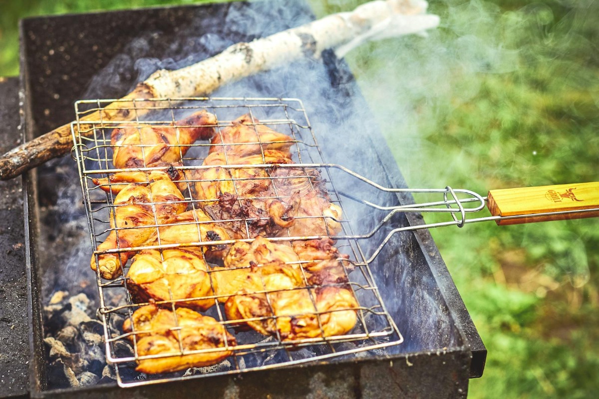 Meat cooking on a smoky grill with visible white smoke - the kind that causes bitter flavor