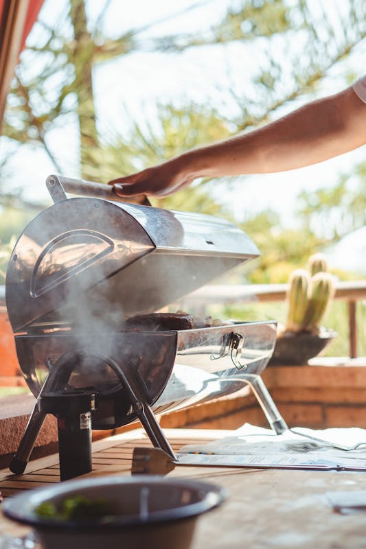 Person opening a pellet grill with smoke rising