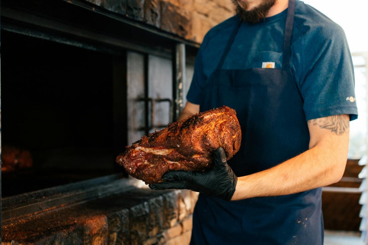 Pitmaster wearing apron holding a freshly smoked piece of meat from the smoker