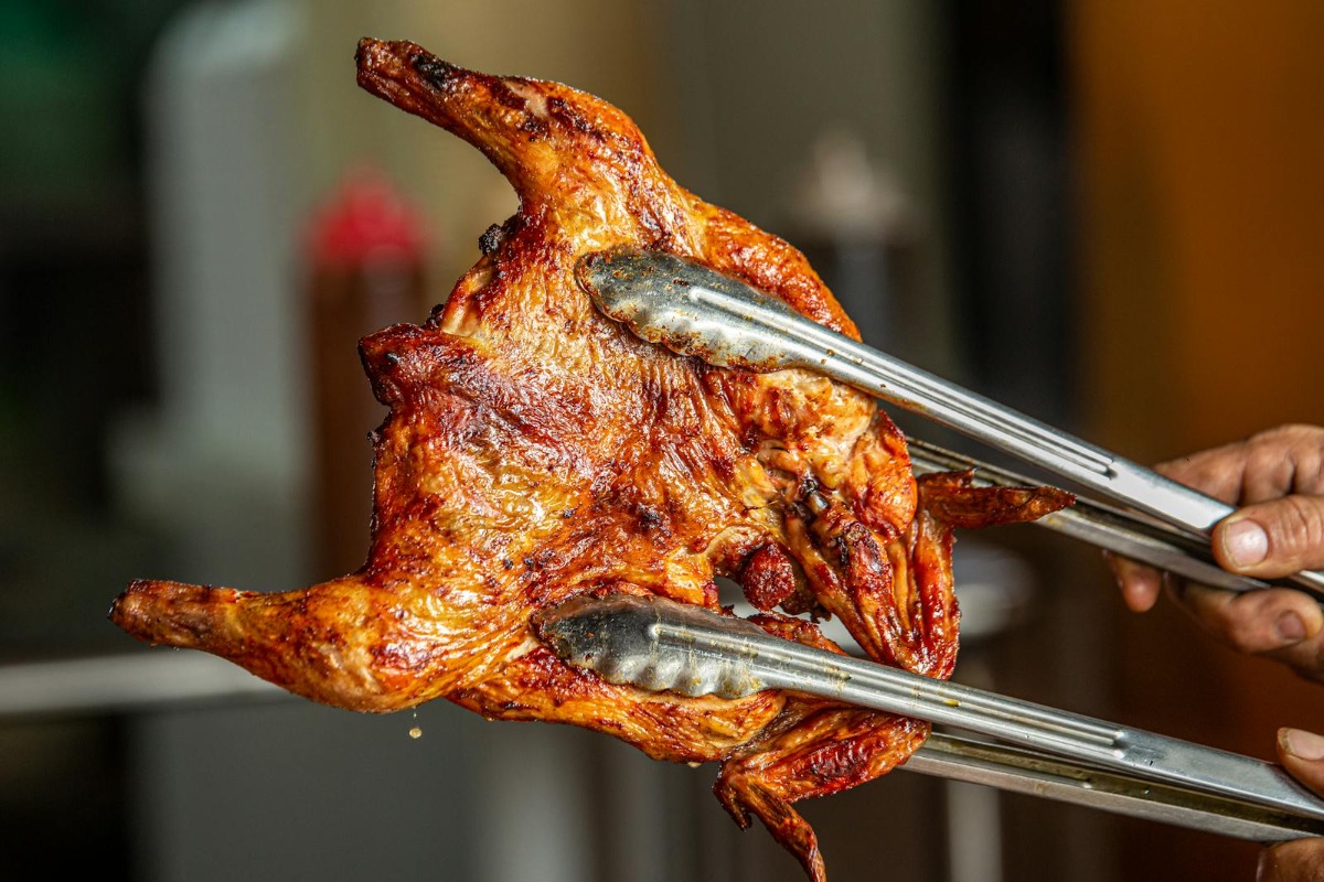 Smoked whole chicken lifted from grill with tongs