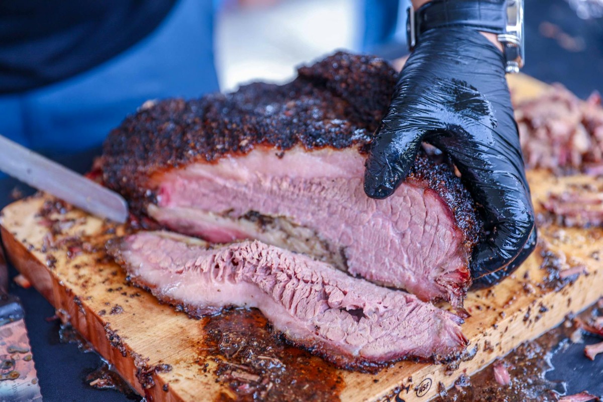 Pitmaster slicing smoked brisket against the grain on a wooden cutting board