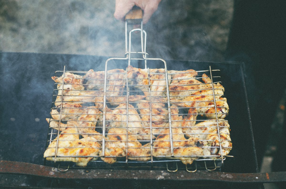 Chicken wings smoking in a grill basket with billowing smoke