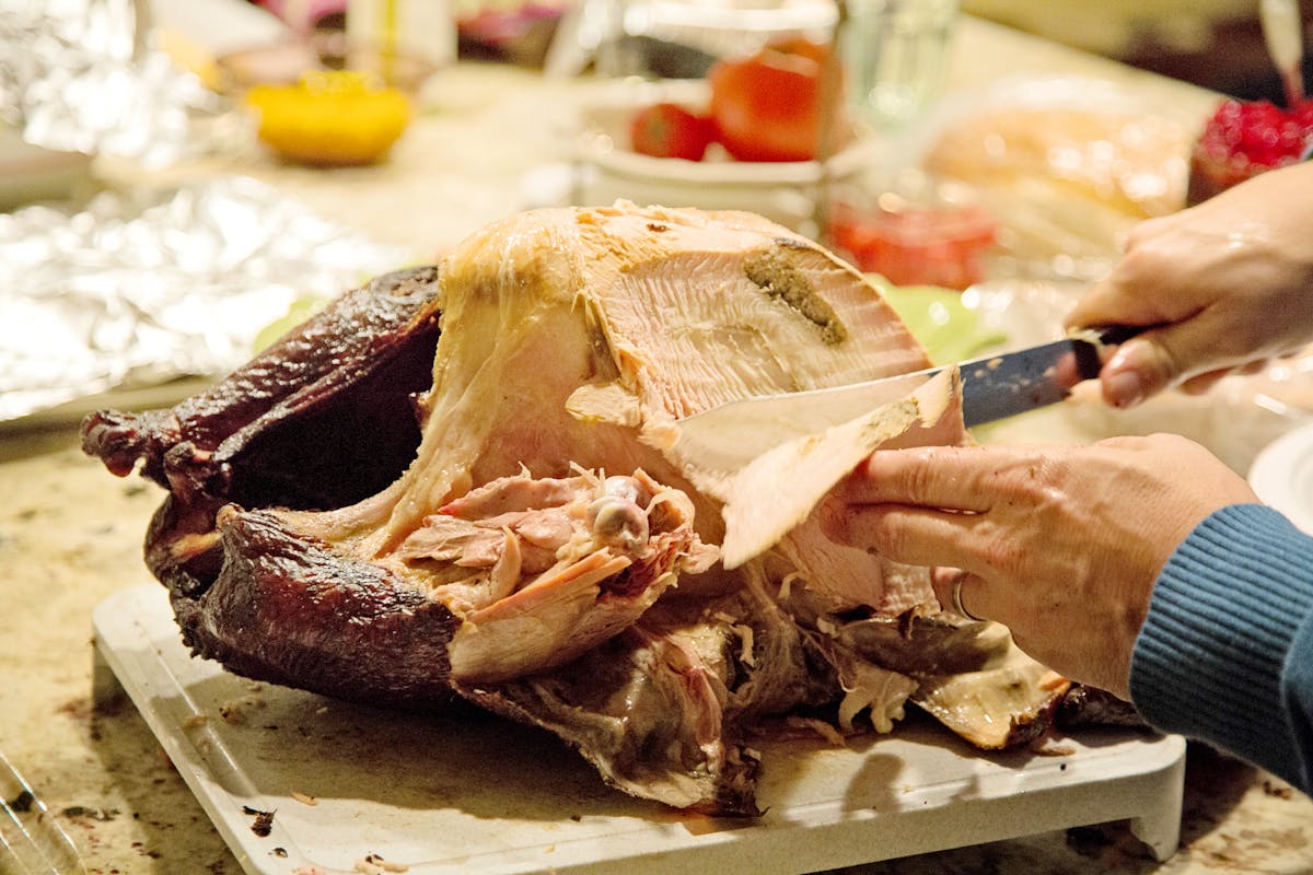Smoked turkey with dark mahogany skin being carved with a knife