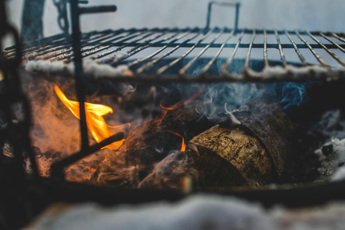 Wood chunks burning with thin blue smoke under a BBQ grill grate